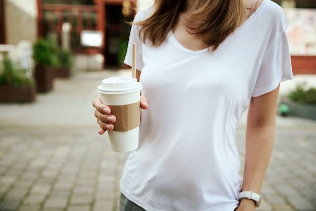 Frau hält Papierkaffeetasse an der Stadtstraße
