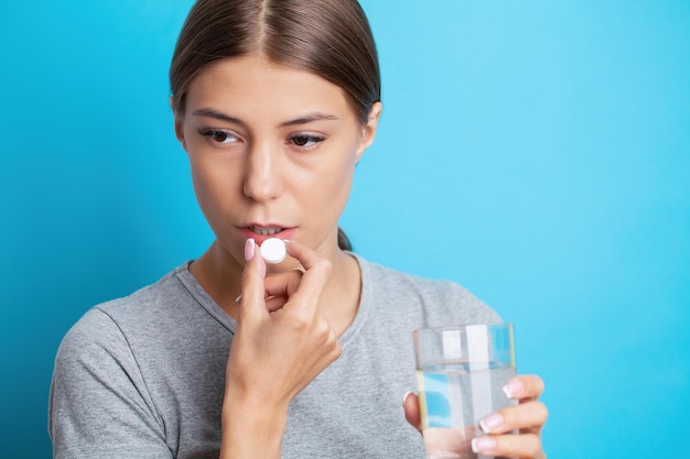 Frau hält Pille und Glas Wasser in der Hand und nimmt Medikamente gegen Kopfschmerzen, Magenschmerzen oder Vitamine