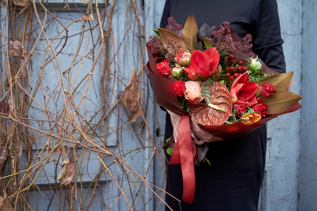 Frau hält schicken Herbstblumenstrauß in den roten Farben in der Weinleseart draußen