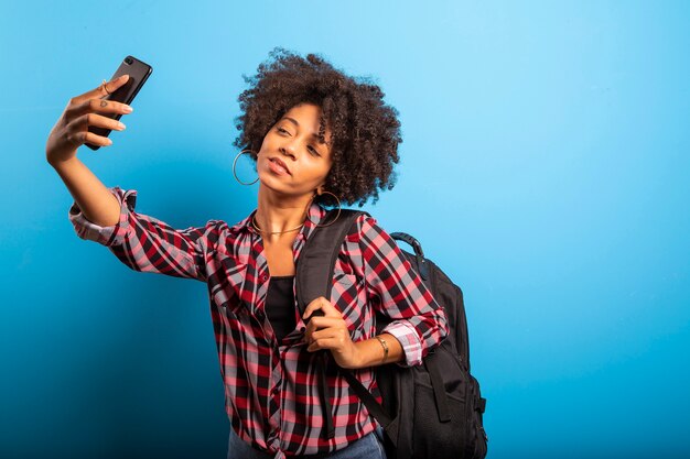 Frau hält Smartphone, das Selfie-Foto auf dem blauen Hintergrund nimmt