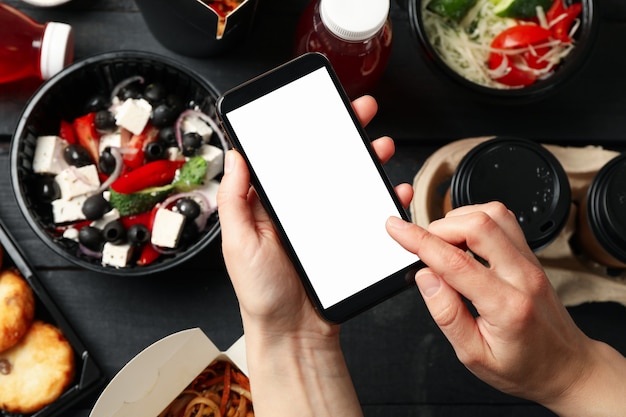 Frau hält Smartphone. Essen in Mitnehmerboxen auf hölzernem Hintergrund