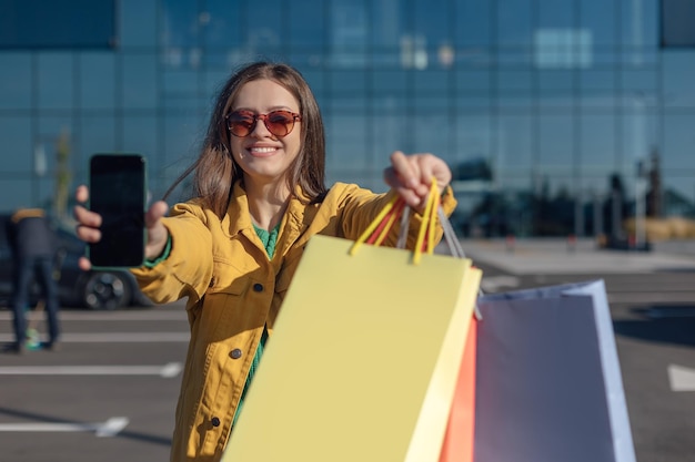 Frau hält Smartphone und Einkaufstüten in der Hand