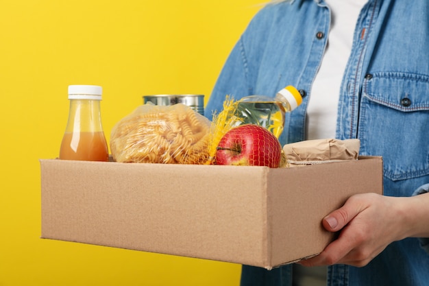 Frau hält Spendenbox auf gelbem Raum. Freiwilligenarbeit