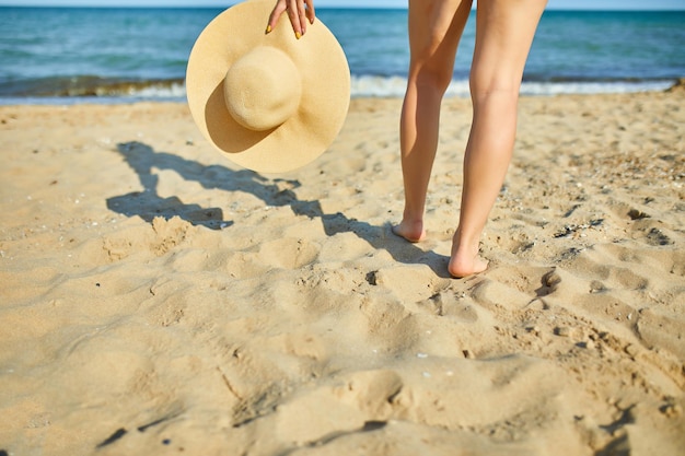 Frau hält Strohhut in der Hand am Strand in der Nähe des Meeres