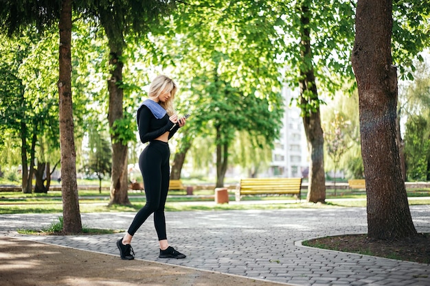 Frau hält Telefon und sucht Musik für Training außerhalb des grünen Parks
