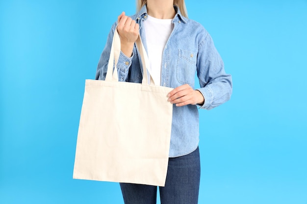 Frau hält weiße Öko-Tasche auf blauem Hintergrund