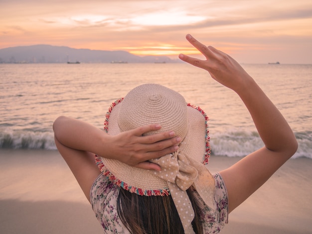 Frau hält zwei Finger oder Victory Sign am Strand während des Sonnenuntergangs