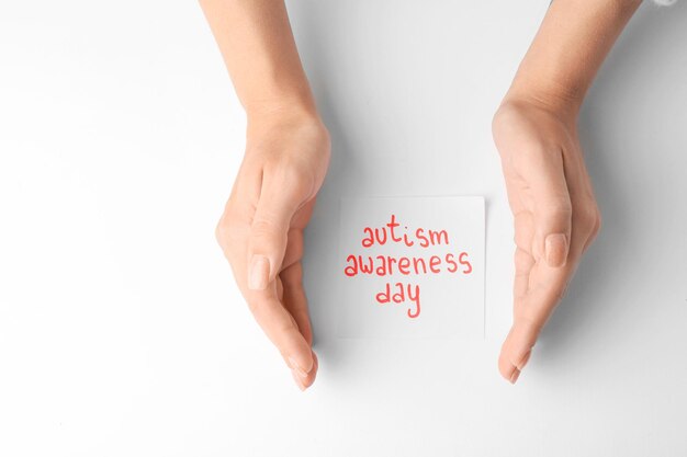 Frau Händchen haltend neben Blatt Papier mit Text AUTISMUS AWARENESS DAY auf weißem Hintergrund