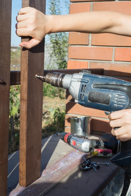 Frau Hände bohren Holzplankenzaun Metallkonstruktion Bau eines Holzzauns mit einem Bohrer und einer Schraube