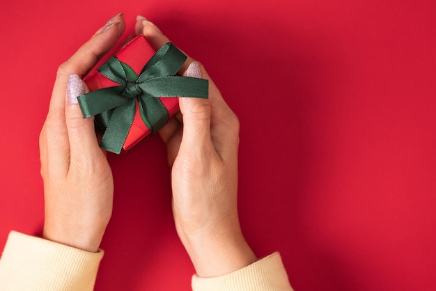 Frau Hände halten Weihnachtsgeschenk Geschenkbox in rotem Papier mit grünem Band eingewickelt