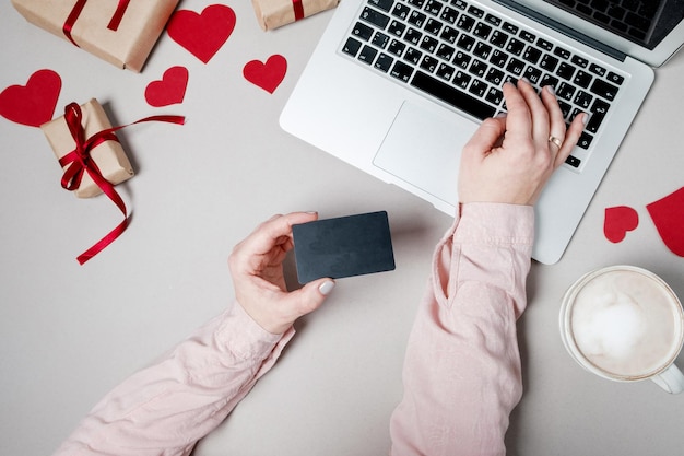 Frau Hände mit Kreditkarte und Laptop Geschenkbox mit Herz und Kaffee auf weißem Hintergrund Valentinstag Online-Shopping-Konzept Urlaub Hintergrund Draufsicht