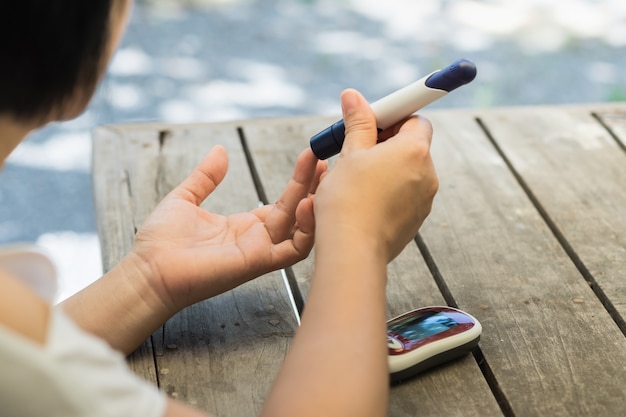 Frau Hände mit Lanzette am Finger, um den Blutzuckerspiegel Diabetes von Glukose-Meter zu überprüfen