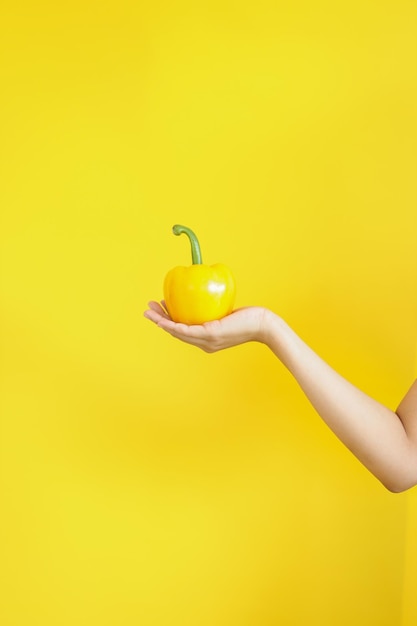 Frau Hand hält frische gelbe Paprika auf gelbem Hintergrund Frisches Gemüse für gesunde Ernährung