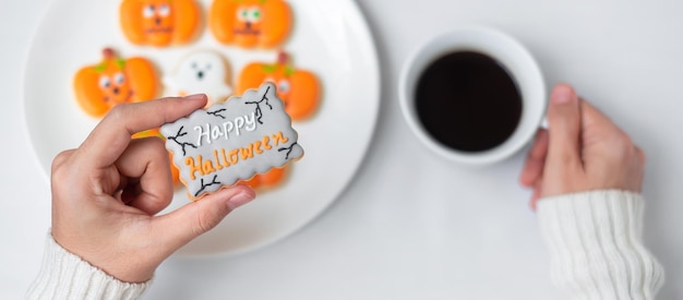 Frau Hand hält lustige Halloween Cookie während des Kaffeetrinkens Happy Halloween Tag Trick or Threat Hallo Oktober Herbst Herbst Traditionelles Party- und Urlaubskonzept