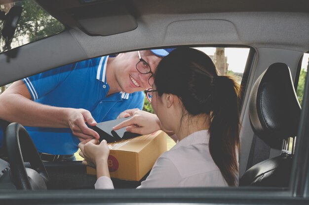 Frau im Auto, das Unterschrift auf Smartphone unterschreibt, um Paket vom Auslieferungsmann zu erhalten