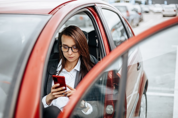 Frau im Auto hinter dem Lenkrad schaut auf das Benachrichtigungstelefon und liest die Nachricht.