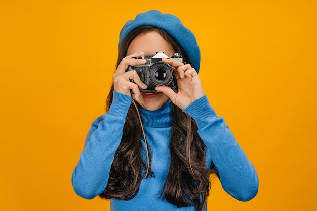 Frau im Baskenmütze fotografiert auf Retro-Kamera isoliert auf gelbem Hintergrund