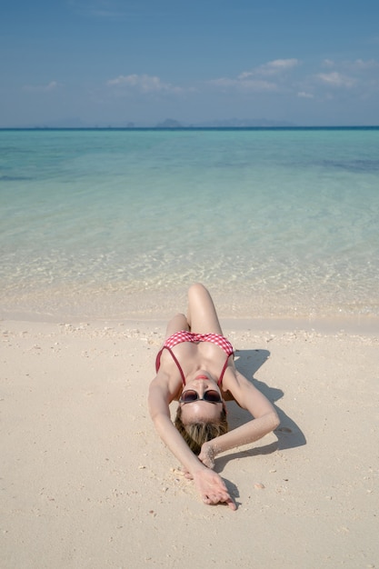 Frau im Bikini, der auf Meerwasser durch weißen Sandstrand liegt. Blaue Meer- und Himmelslandschaft. Sommerurlaub.