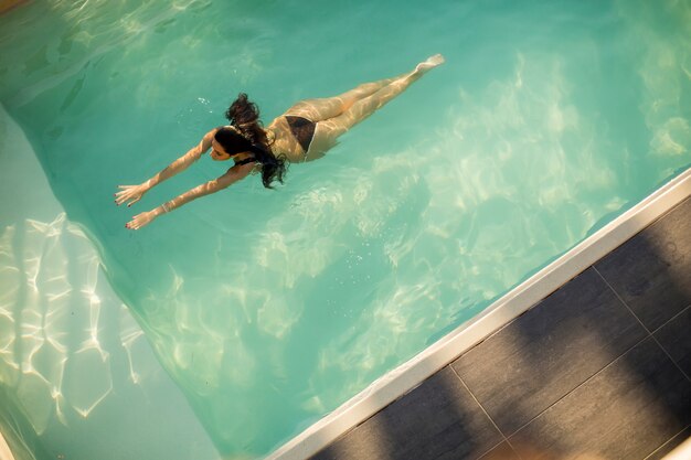 Frau im Bikini, der auf Wasser im Pool am Sommertag schwimmt