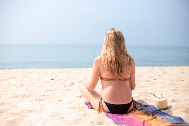 Frau im Bikini sitzt auf dem Sand am Strand in der Lotussitz