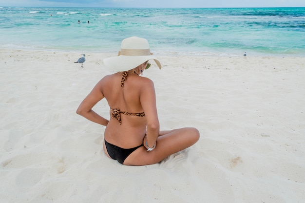 Frau im Bikini sitzt auf dem Sand.