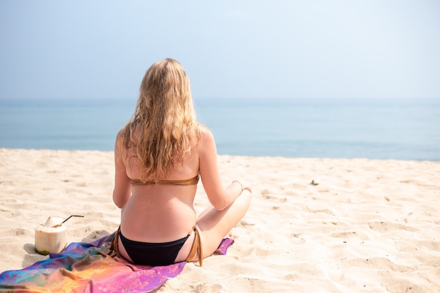 Frau im Bikini sitzt im Sand am Strand