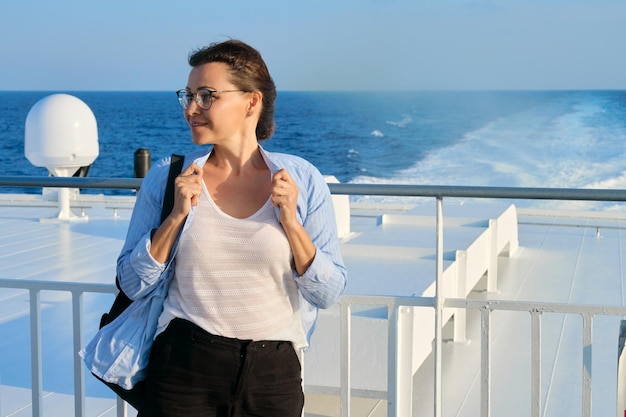 Frau im blauen Hemd auf dem Deck des Schiffes mit Blick auf den Sonnenuntergang am Meer