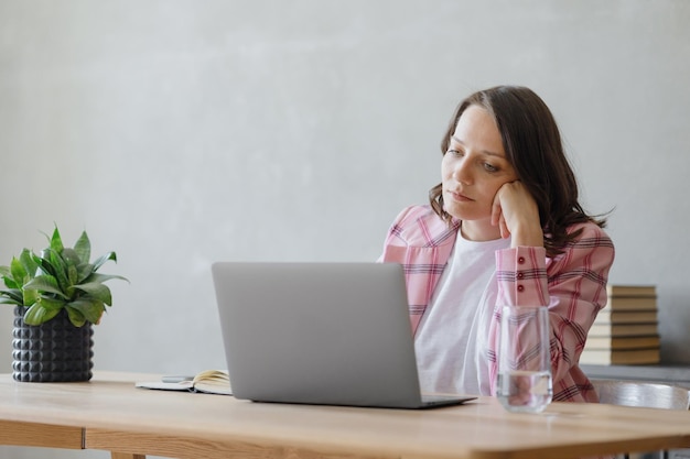 Frau im Büro arbeitet oder schaut nachdenklich in die Ferne, eine schöne europäische Geschäftsfrau in einer rosa Jacke sitzt an einem Schreibtisch