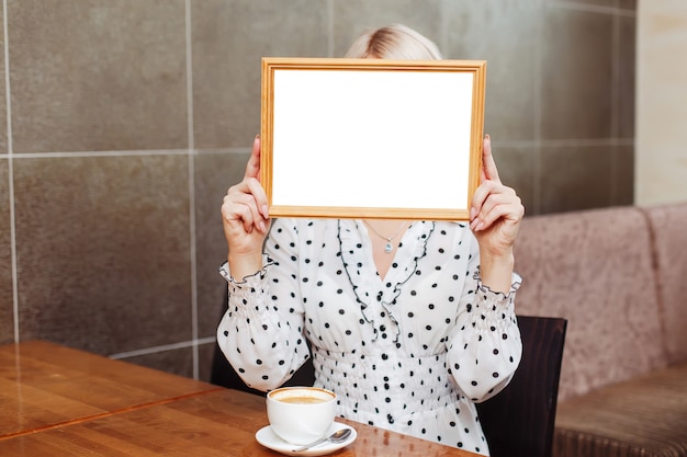 Frau im Café, das Holzrahmen, leeres weißes Modell hält