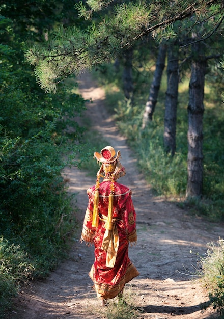 Frau im chinesischen Prinzessinnenkostüm, die von hinten in den Pinienwald geht