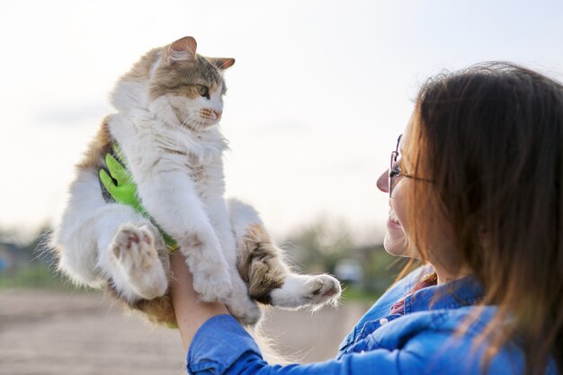 Frau im Freien, die Hauskatze in den Armen hält und mit ihr spricht, Freundschaft des Besitzers und des Haustieres