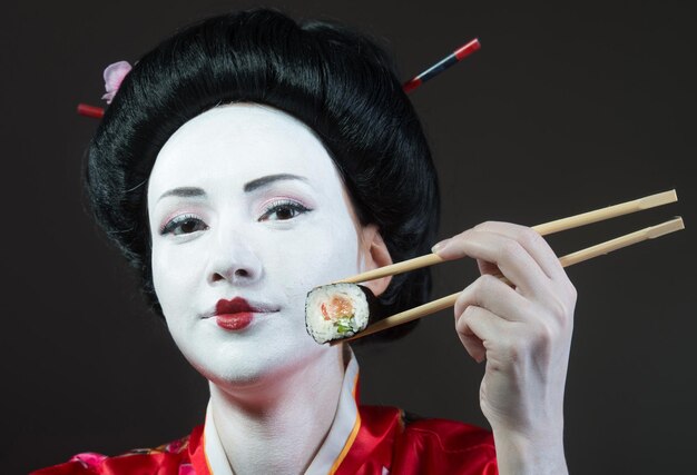 Frau im Geisha-Make-up, das Sushi grauen Hintergrund isst