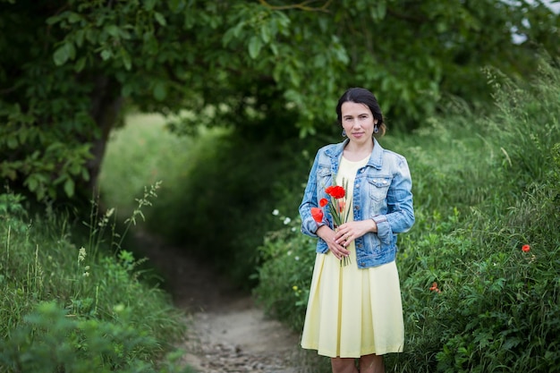 Frau im gelben Kleid, die Mohn und Wildblumen sammelt, die auf einer Sommerwiese spazieren gehen