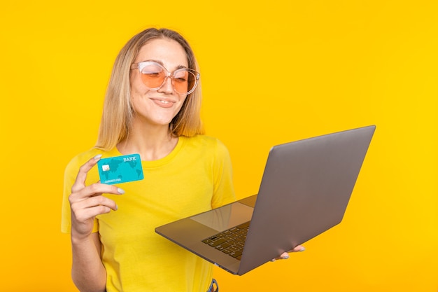Frau im gelben T-Shirt, das online mit Kreditkarte und Computer auf Gelb einkauft