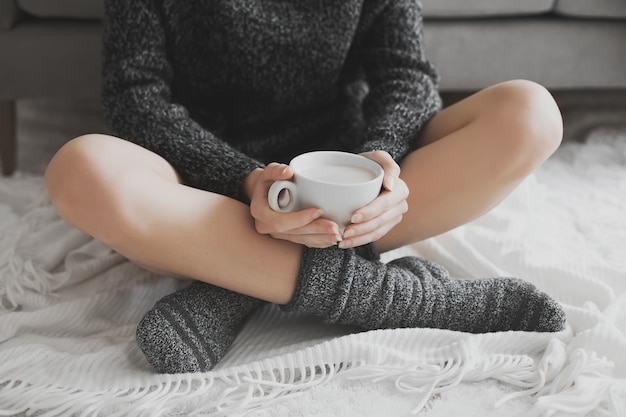 Frau im gemütlichen Raum mit Tasse Kakao in der Hand.