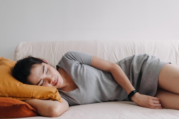 Frau im grauen Kleid schläft und entspannt auf dem Sofa in der Wohnung