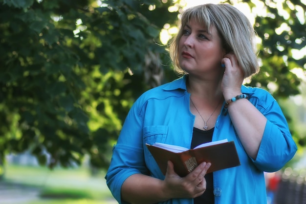 Frau im grünen Baum des Parks mit Buch