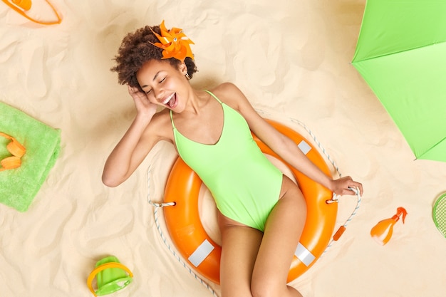 Frau im grünen Bikini posiert auf aufgeblasenem Rettungsring hält den Mund offen schließt die Augen verbringt Freizeit am Strand mag den Sommer. Menschen Urlaub Entspannungskonzept