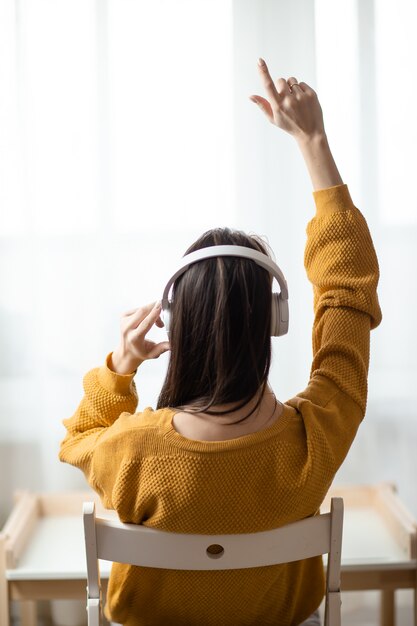 Frau im Heimbüro während der Selbstisolation, die von zu Hause aus arbeitet. Online-Bildung, E-Learning während der Quarantäne. Frau hört Musik in weißen kabellosen Kopfhörern.