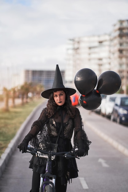 Frau im Hexenkostüm mit schwarzen Luftballons, die auf dem Straßenporträt Fahrrad fahren