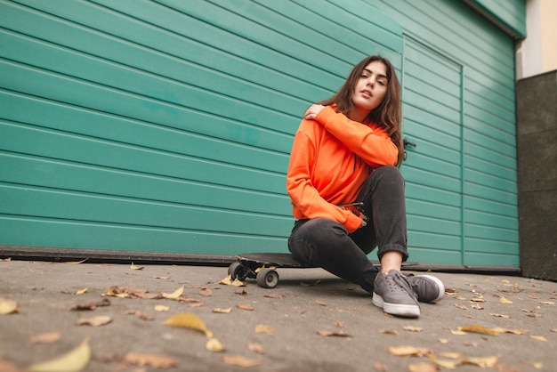 Frau im Hoodie steht mit einem Longboard