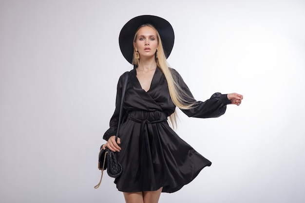 Frau im hübschen schwarzen Kleid Hut High Heels Tasche Weißer Hintergrund Studio Shot Portrait Blond