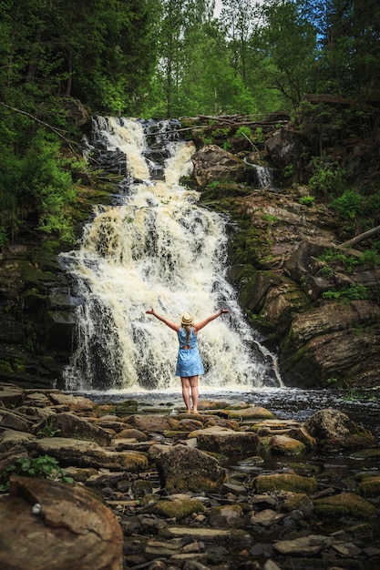 Frau im Hut, die Natur nahe dem Waldwasserfall genießt.