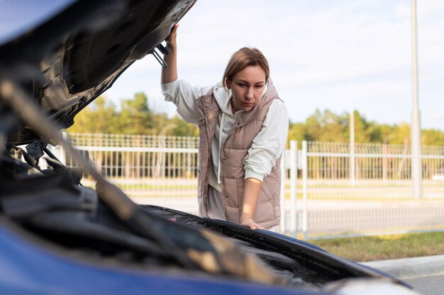 Frau im islamischen miesen auto mit aufgesetzter motorhaube, die versucht, die ursache für den zusammenbruch des autos zu finden