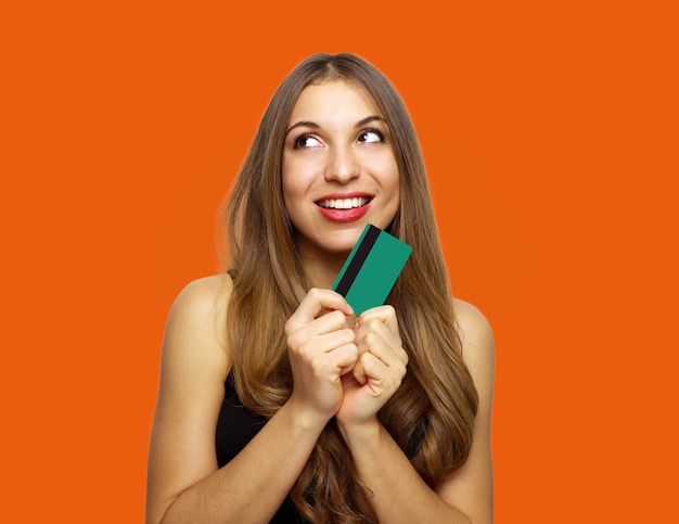 Frau im Kleid hält Kreditkarte und schaut weg über orange Hintergrund