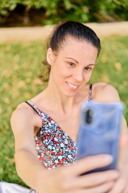 Frau im Kleid lächelt und macht ein Selfie auf dem Rasen