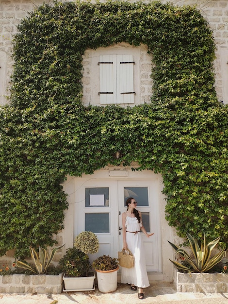 Frau im Kleid steht in der Nähe des mit Pflanzen bedeckten Gebäudes in der Altstadt von Perast