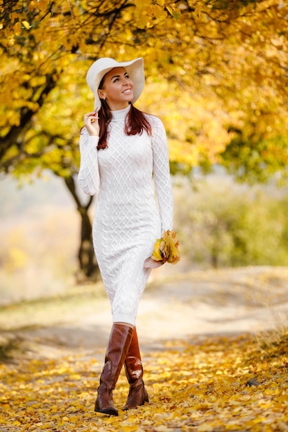 Frau im Kleid und im Hut auf Hintergrund des Herbstlaubs