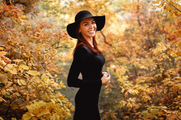 Frau im Kleid und im Hut auf Hintergrund des Herbstlaubs