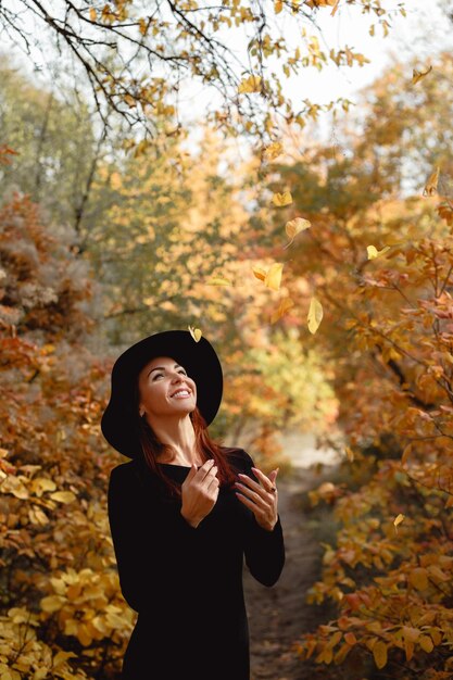 Frau im Kleid und im Hut auf Hintergrund des Herbstlaubs